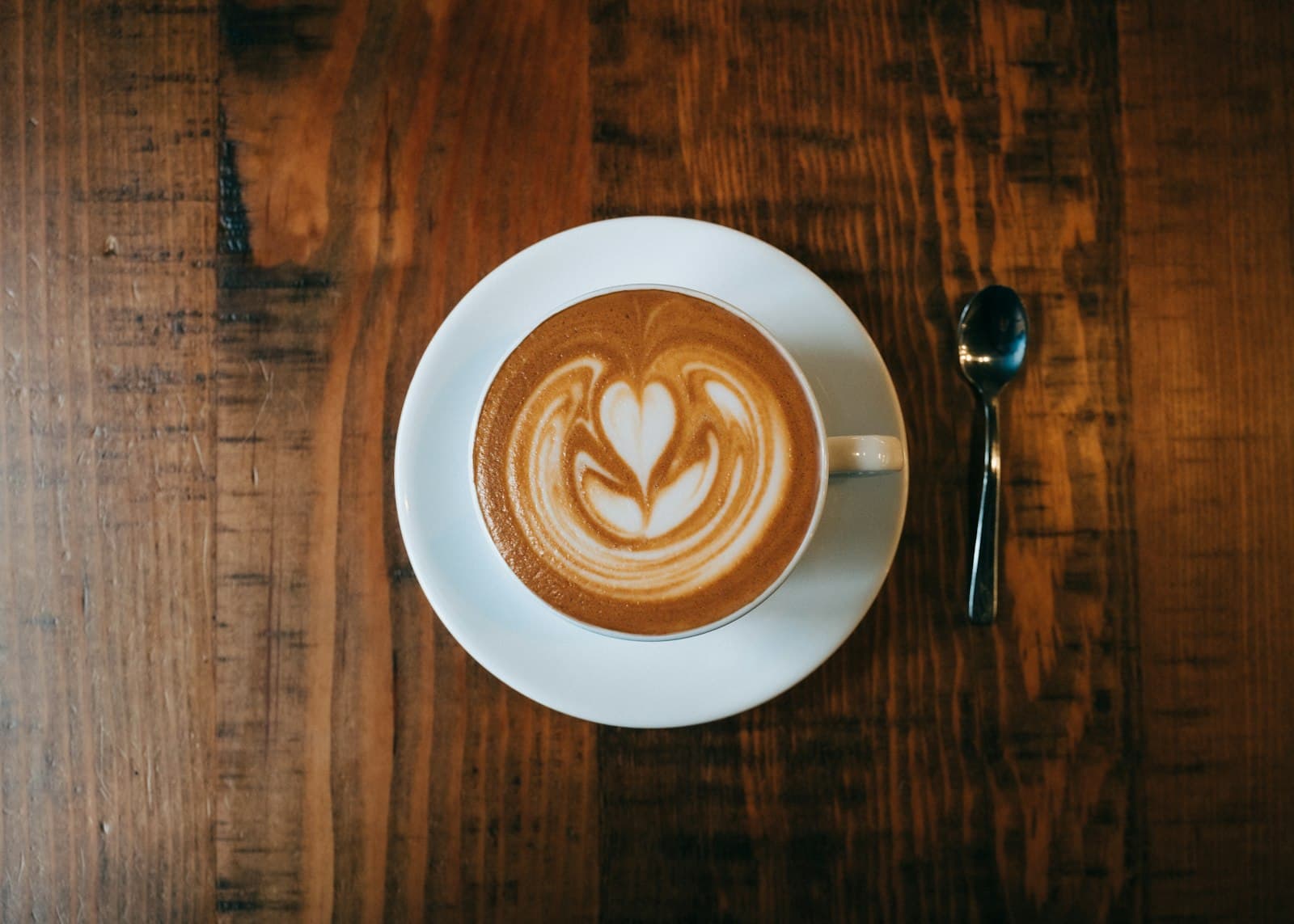 Cappuccino met latte-art op een schotel, van bovenaf op een houten tafel