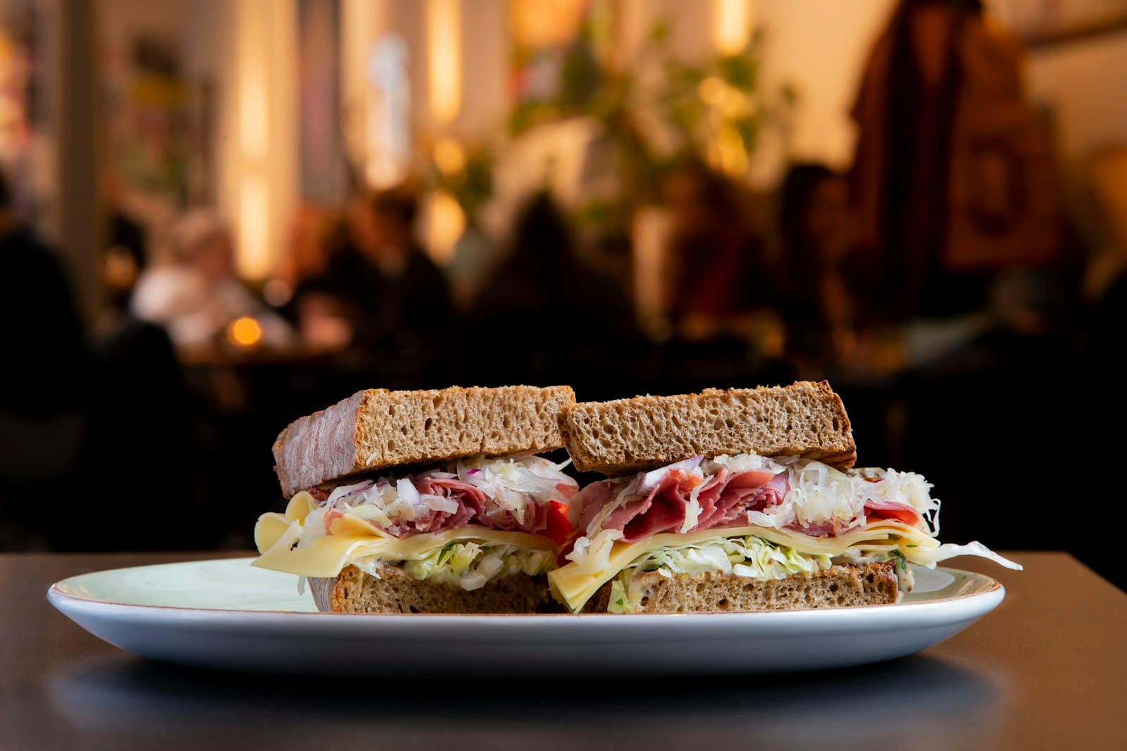 Doorgesneden broodje op roggebrood met pastrami, zuurkool en kaas op een wit bord