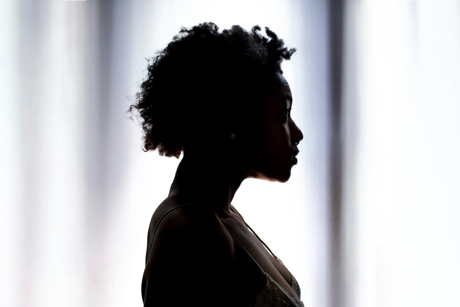 Vrouw in profiel als donker silhouet voor een lichte, zacht geplooide achtergrond